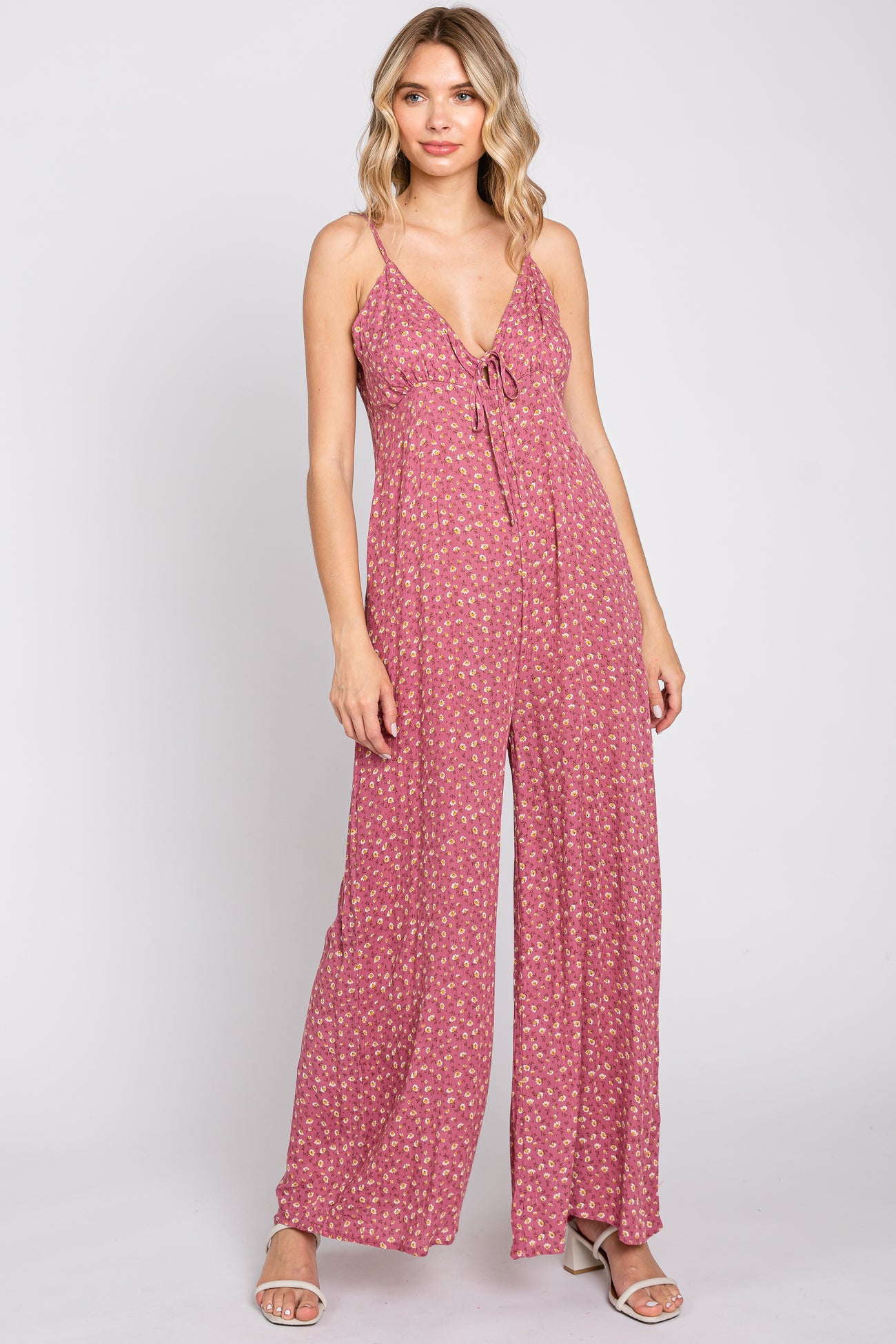 woman wearing a pink floral print wide leg jumpsuit with spaghetti straps and tie front detail