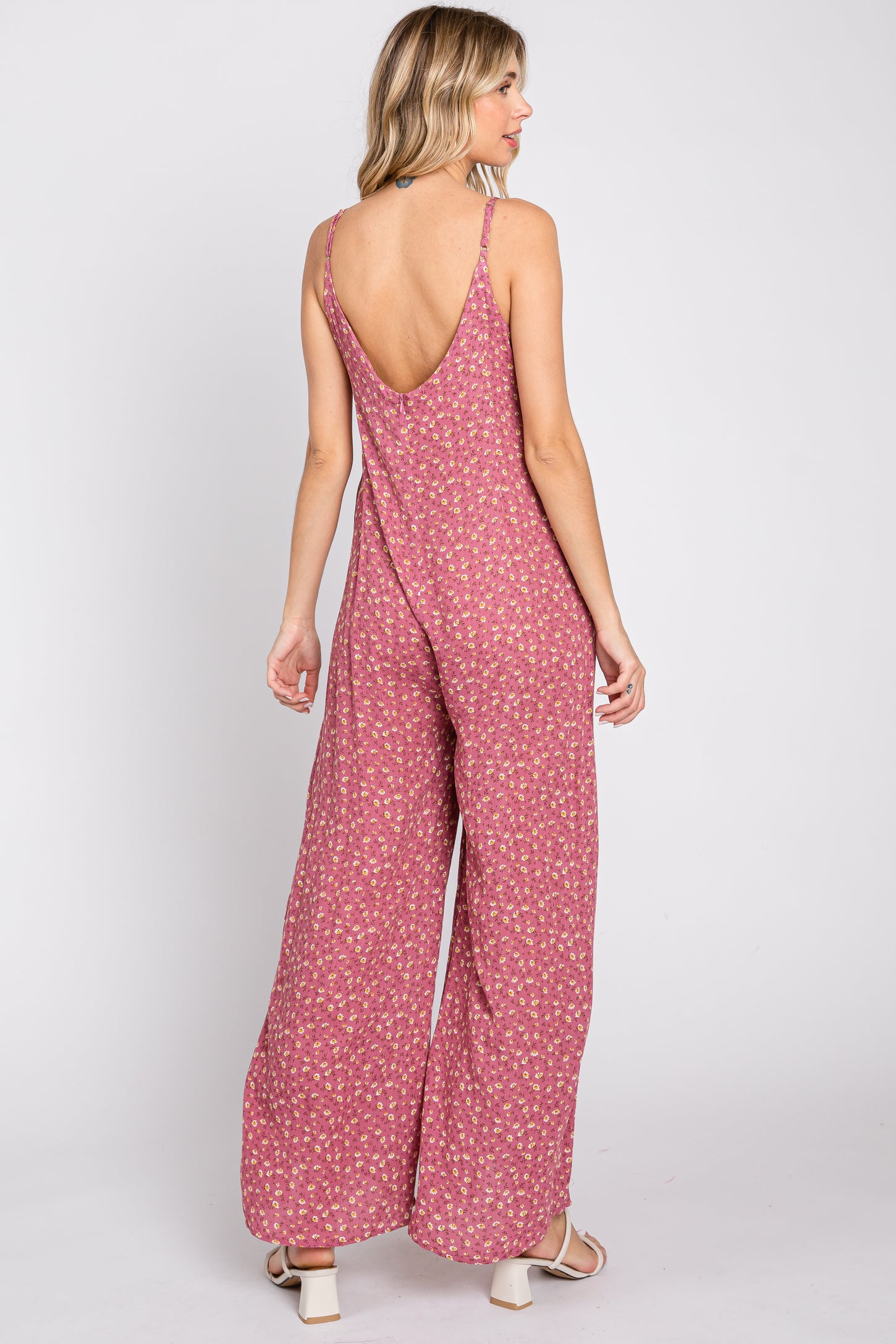 woman wearing a pink floral print jumpsuit with a low back and wide legs, seen from the back