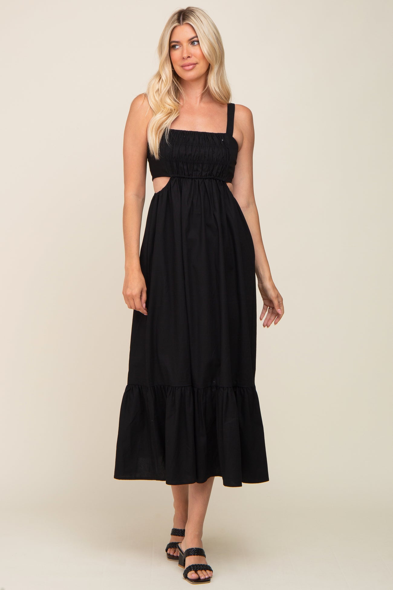 woman wearing a black sleeveless midi dress with side cutouts and a tiered hem