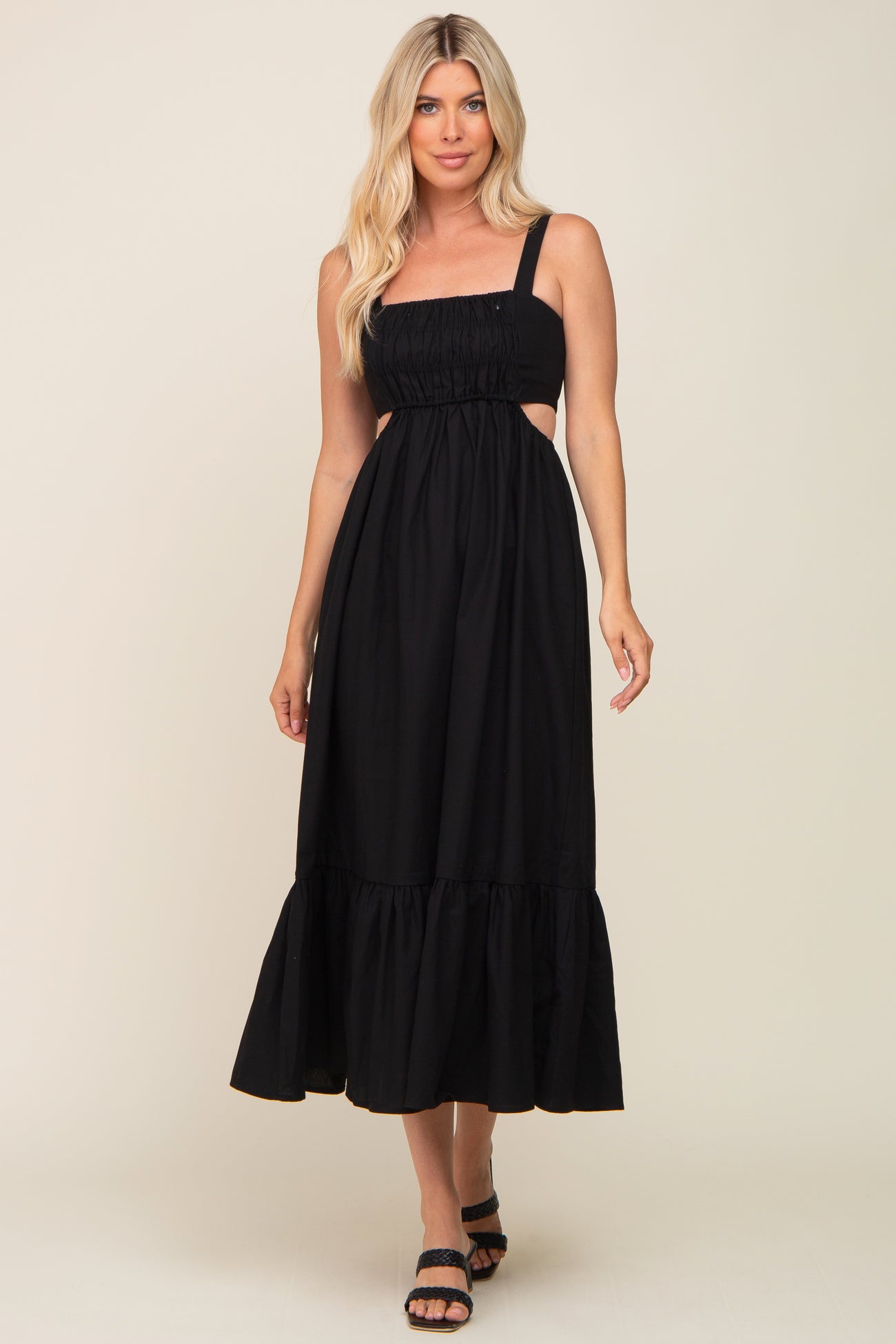 Woman wearing a black sleeveless midi dress with side cutouts and a ruffled hem against a neutral background