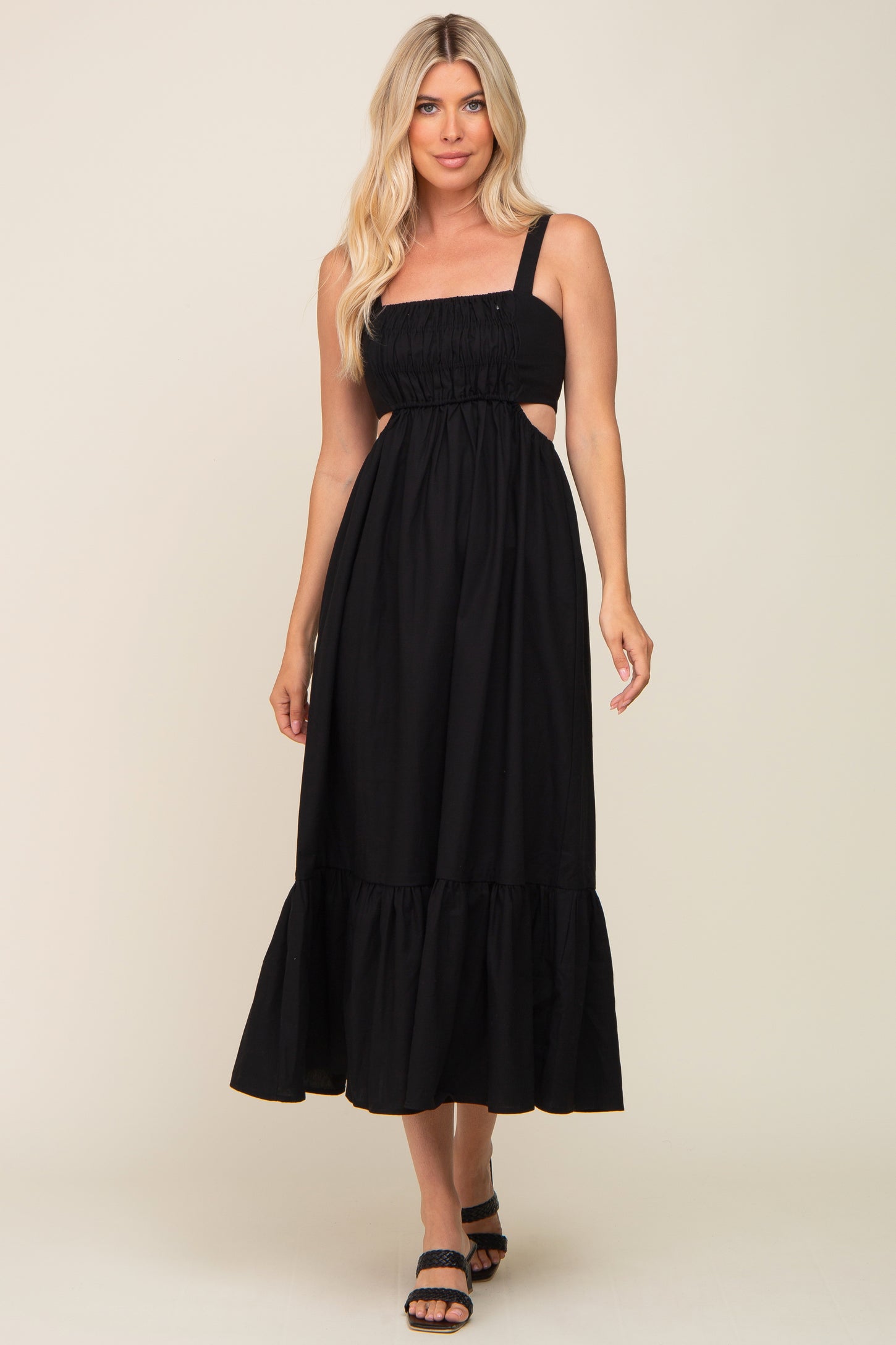 Woman wearing a black sleeveless midi dress with side cutouts and a ruffled hem against a neutral background