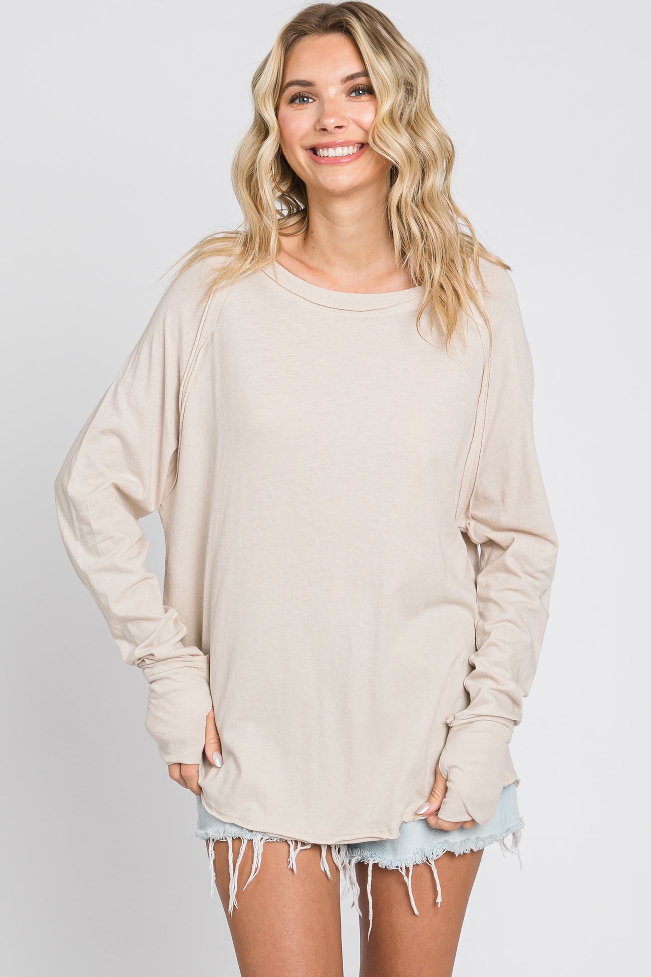 woman wearing a beige long sleeve oversized top with rolled cuffs and distressed denim shorts