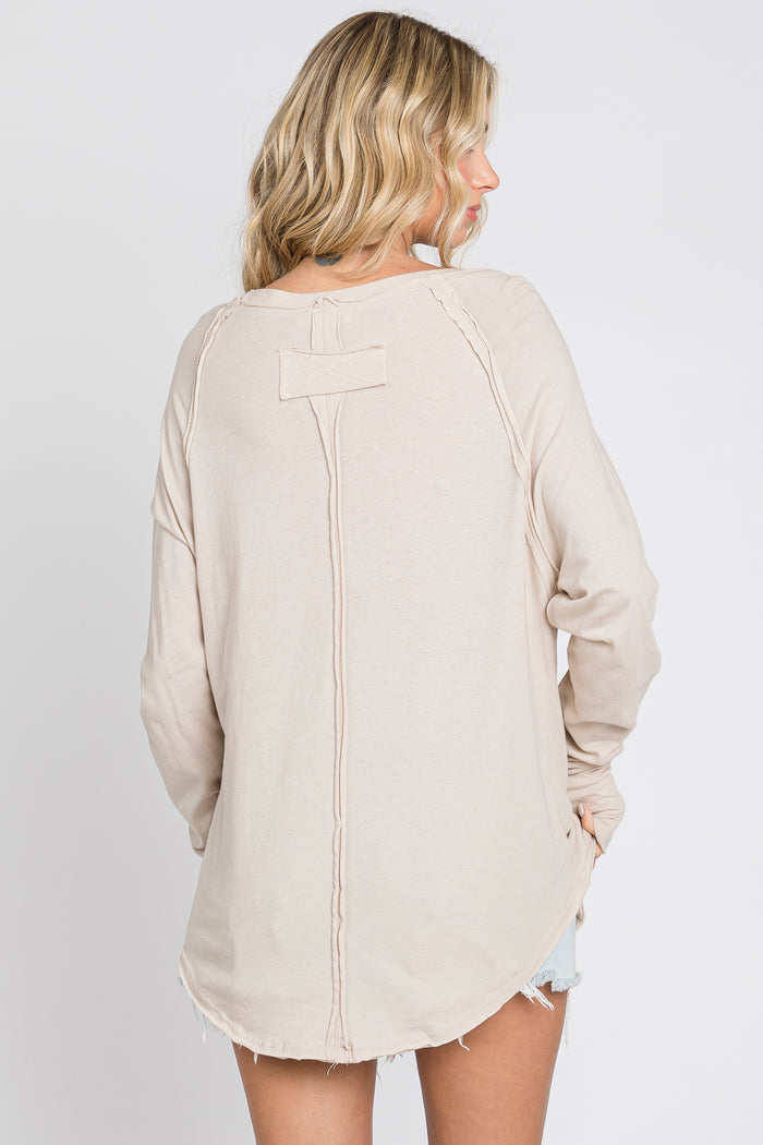 woman wearing a beige long sleeve top with a round hem and seam detailing on the back
