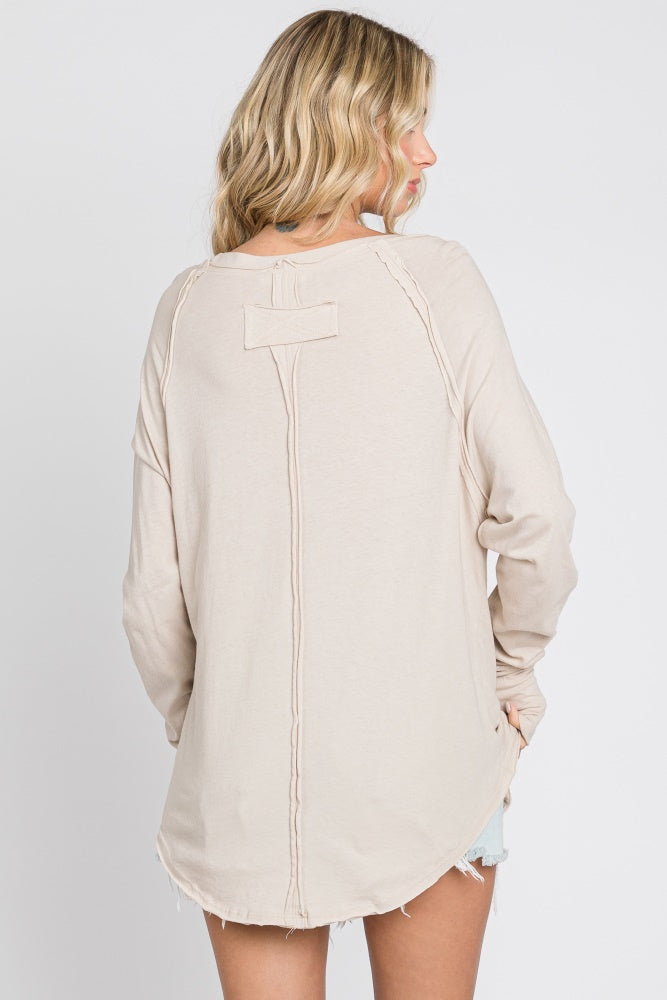woman wearing a beige long sleeve top with a round hem and seam detailing on the back
