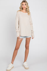 woman wearing a beige long sleeve top with loose fit and ripped denim shorts, styled with white sneakers