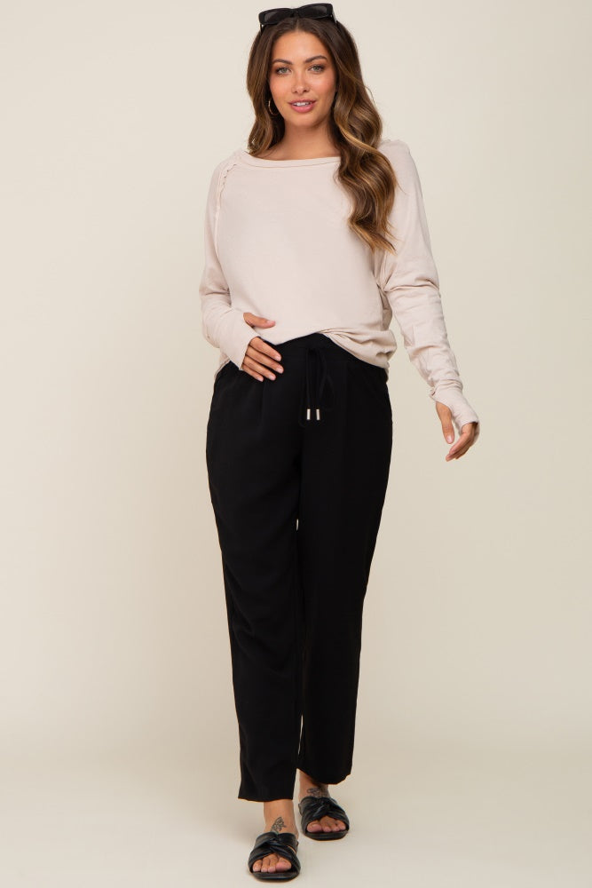 woman wearing a beige long sleeve maternity top and black drawstring maternity pants, showing her baby bump