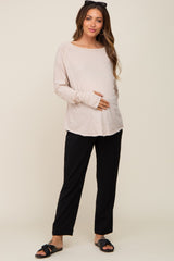 woman wearing a light pink long sleeve maternity top and black pants, holding her baby bump