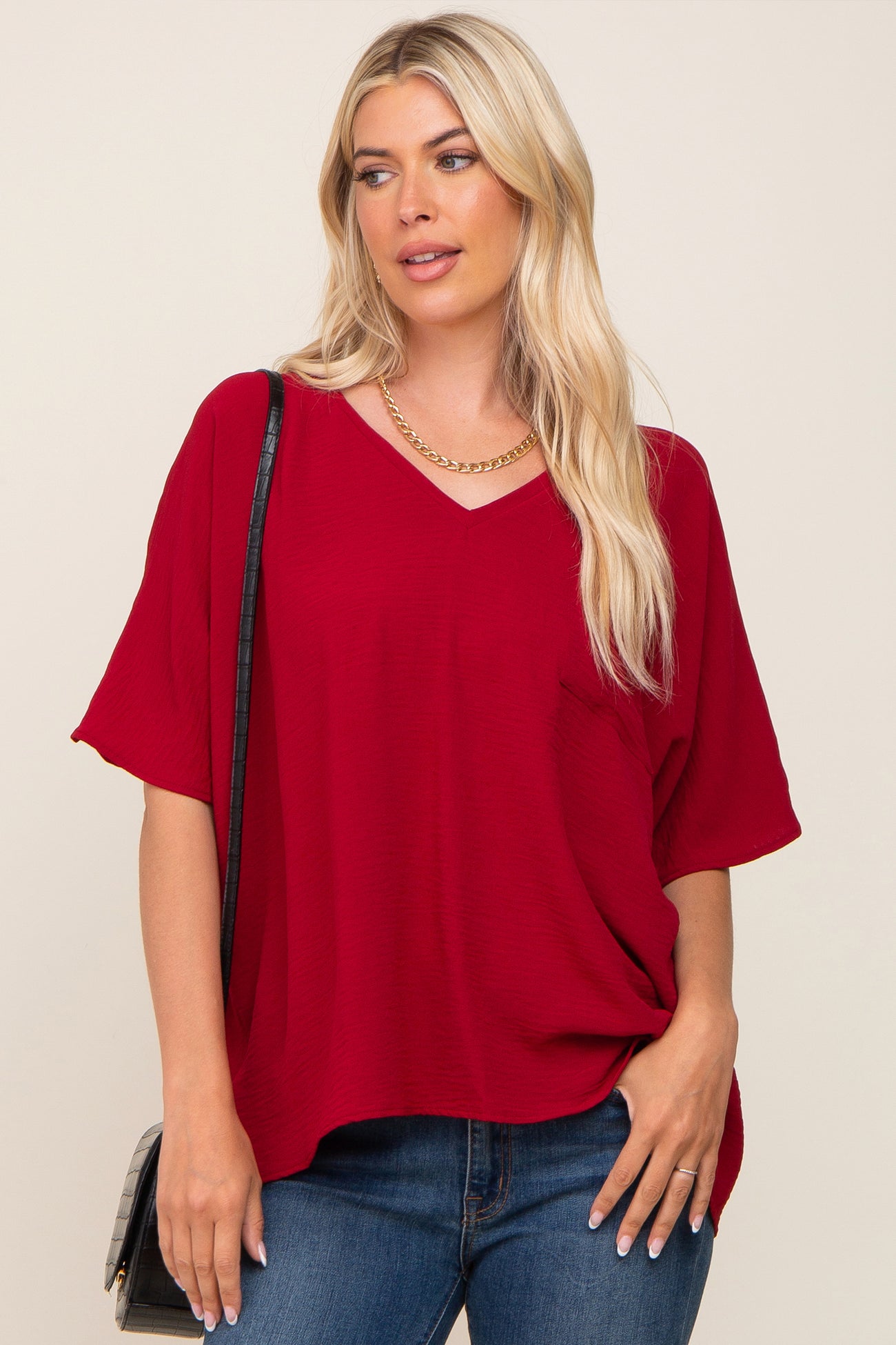 woman wearing a red v-neck oversized top with short sleeves and a pocket, paired with blue jeans