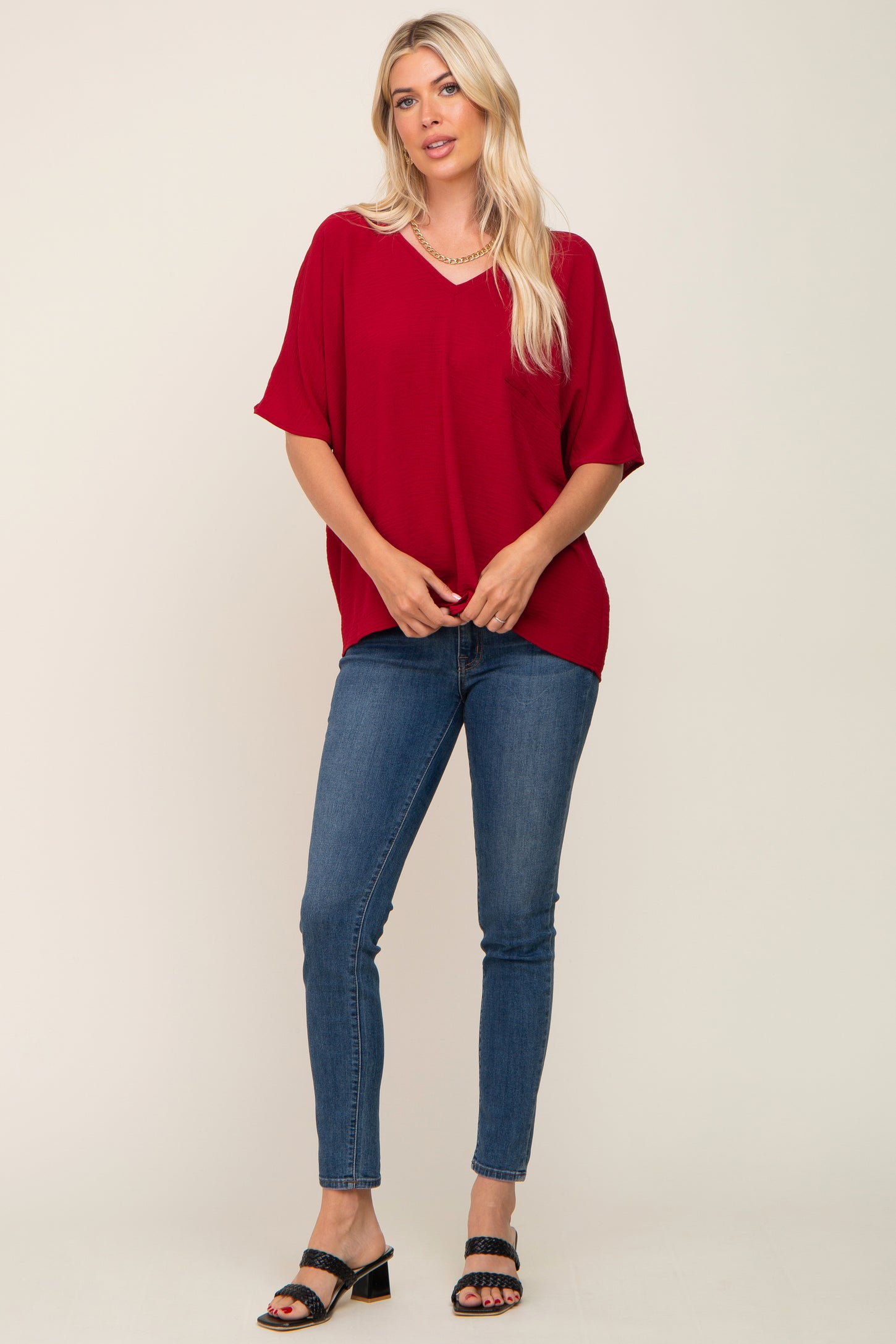 woman wearing a red short sleeve top with a v-neck and blue skinny jeans, standing and posing with one hand on her hip
