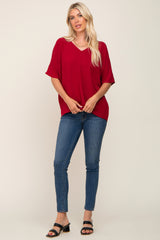 woman wearing a red short sleeve top with a v-neck and blue skinny jeans, standing and posing with one hand on her hip