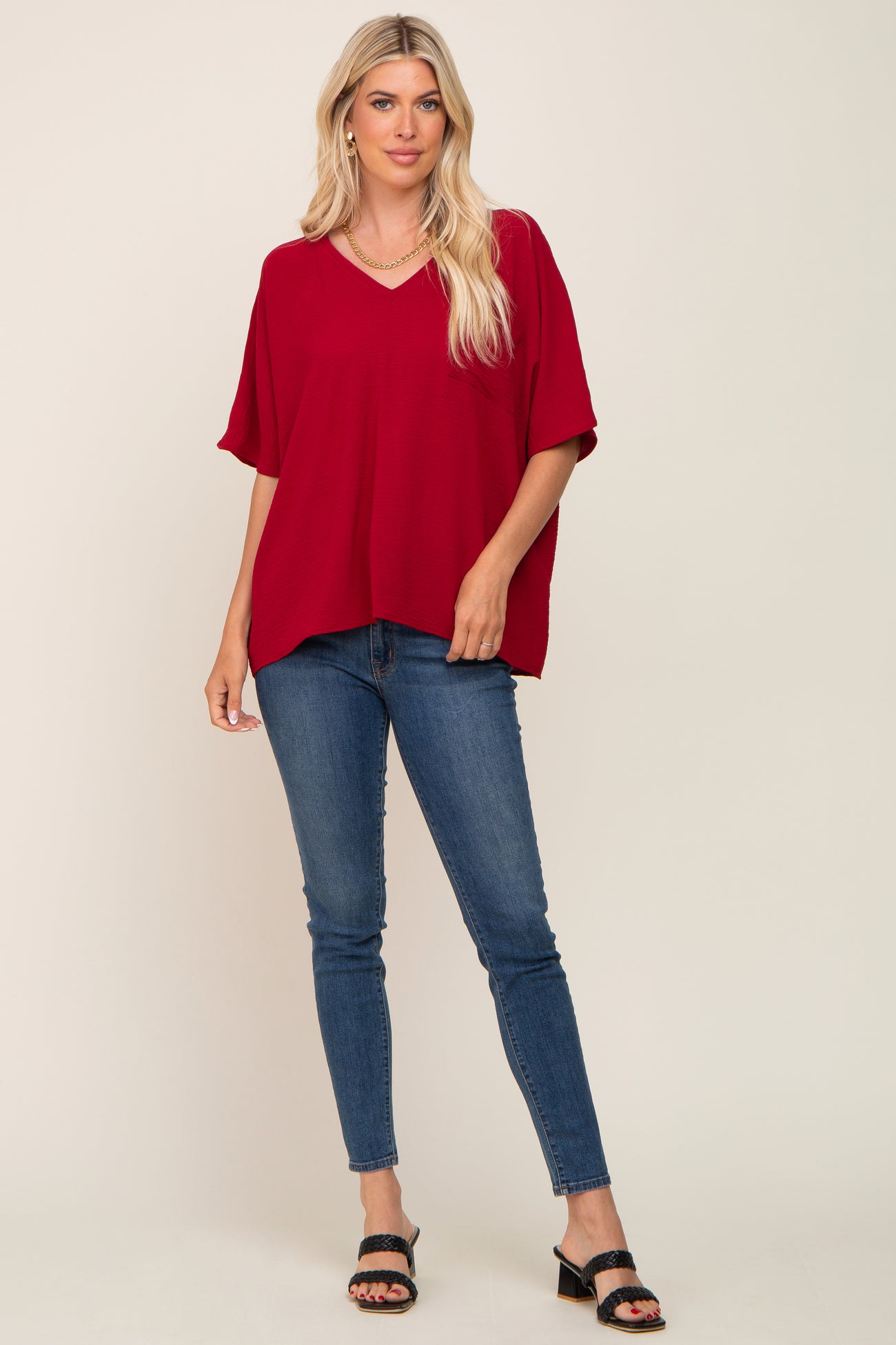 woman wearing a red v-neck oversized top with short sleeves paired with skinny jeans and sandals