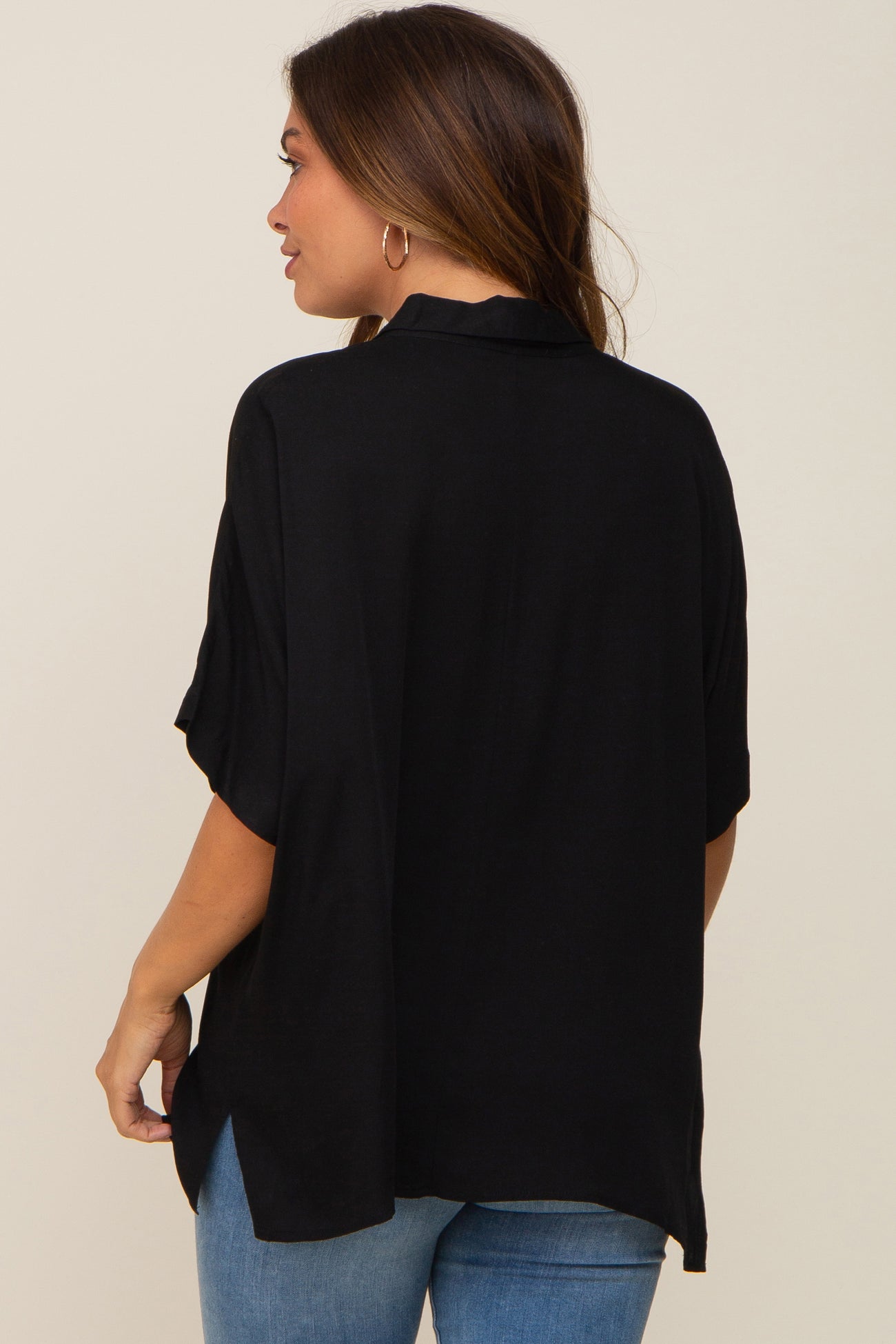 woman wearing a black short sleeve maternity top, shown from the back with side slits, paired with blue jeans