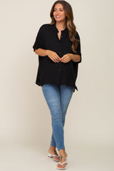 woman wearing a black maternity top with buttons, paired with blue skinny jeans and white sandals, standing confidently