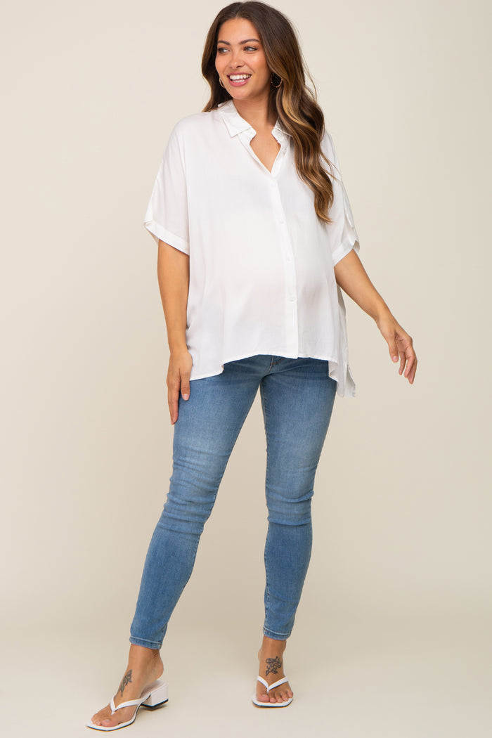 woman wearing a white short sleeve maternity top and blue skinny jeans, showing her baby bump