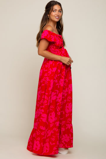 woman wearing a red floral off-the-shoulder maternity maxi dress and holding her baby bump