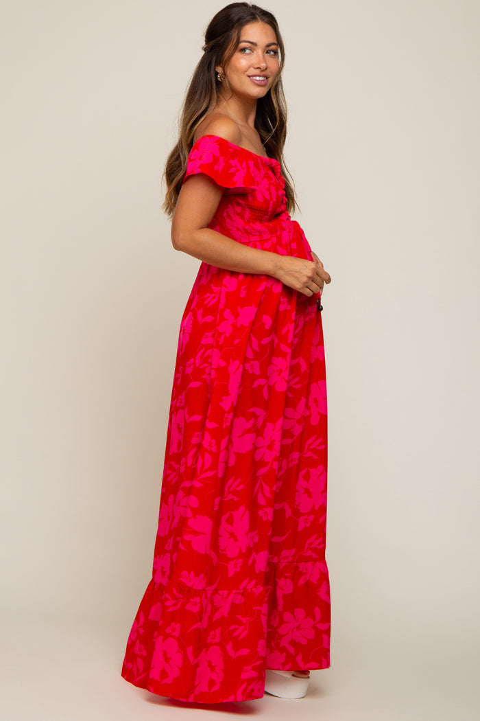 woman wearing a red floral off-the-shoulder maternity maxi dress and holding her baby bump