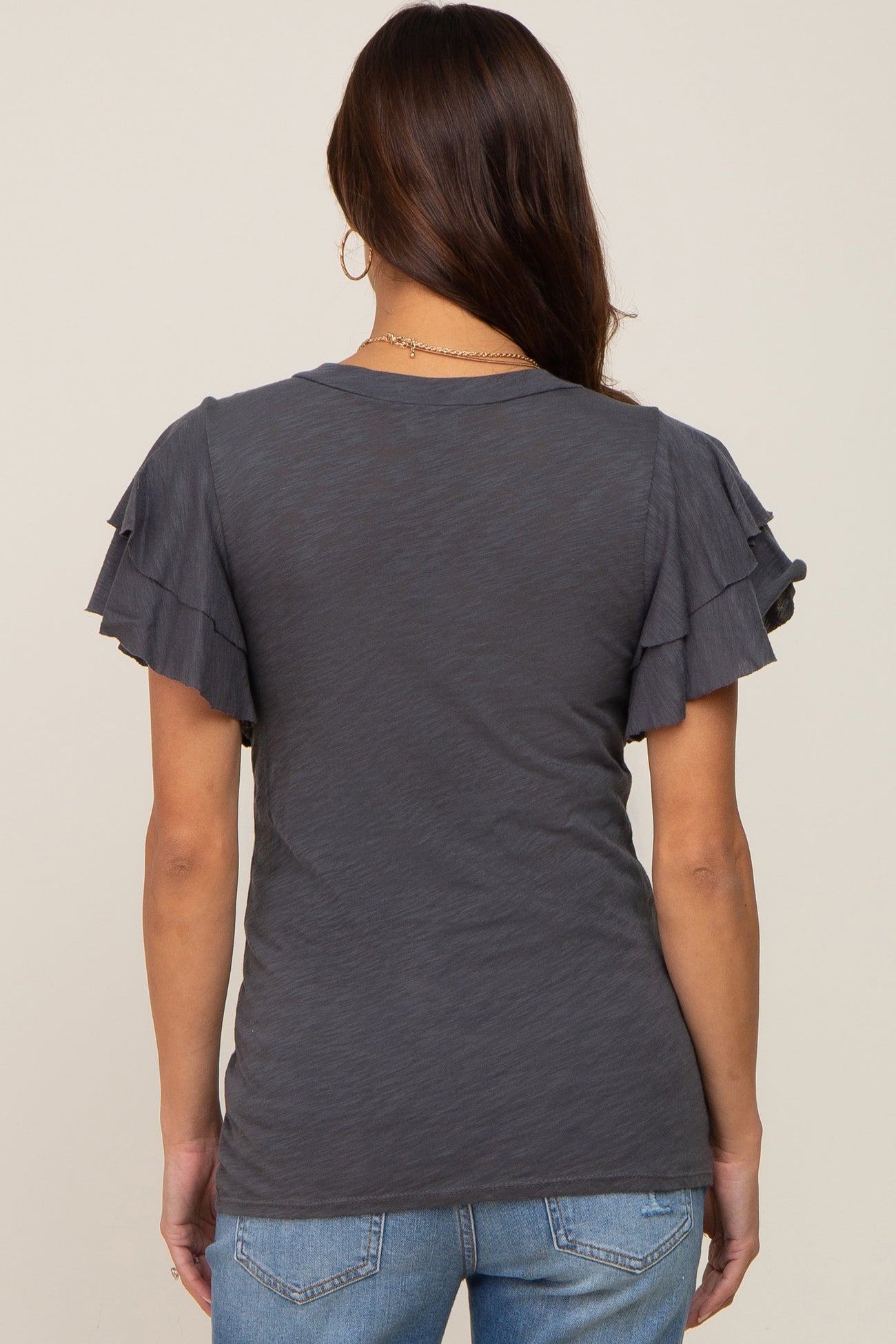 Back view of a woman wearing a charcoal grey t-shirt with tiered ruffle sleeves and blue jeans