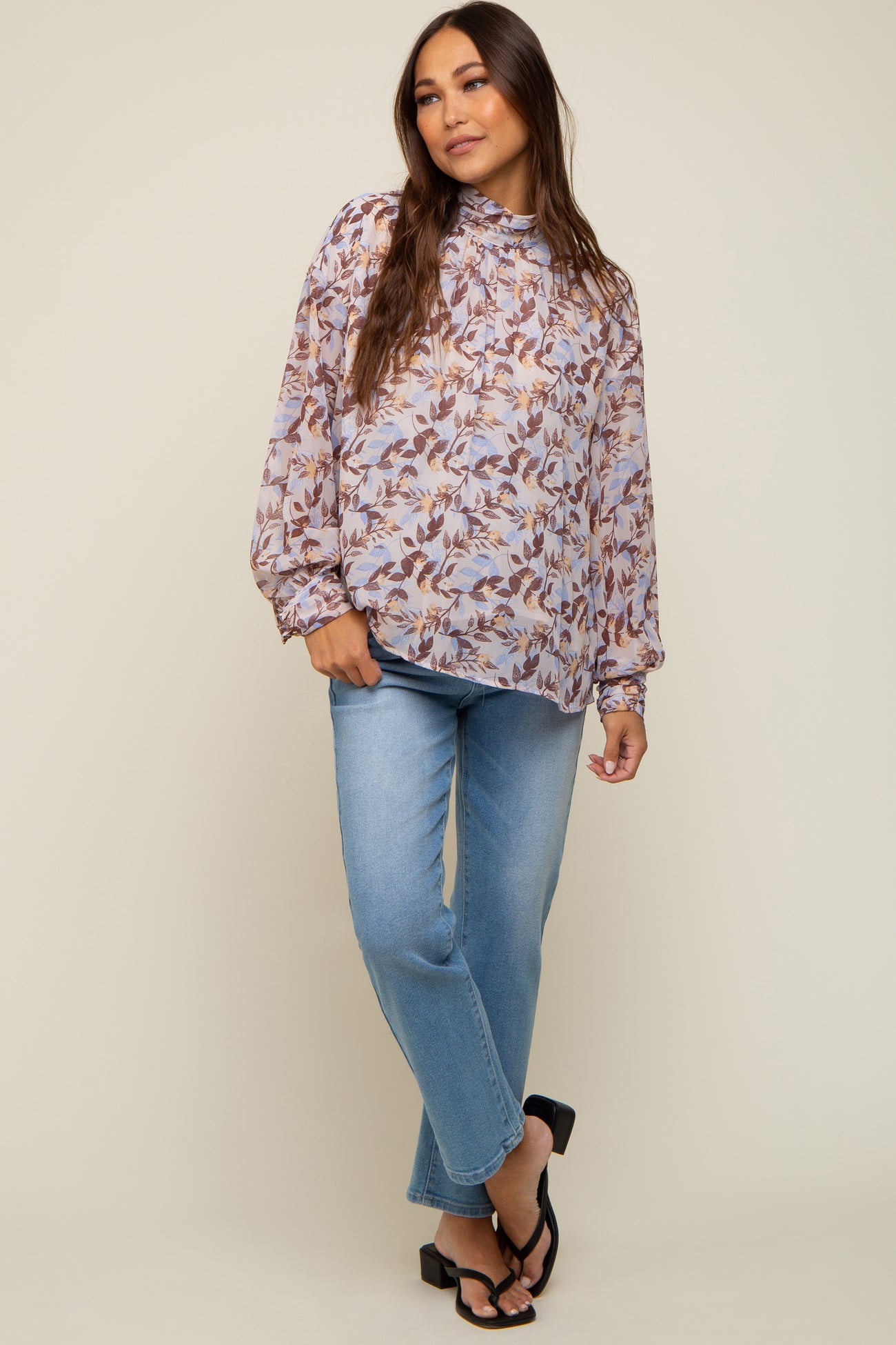 Woman wearing a floral high-neck long sleeve blouse and light wash straight leg jeans with black sandals
