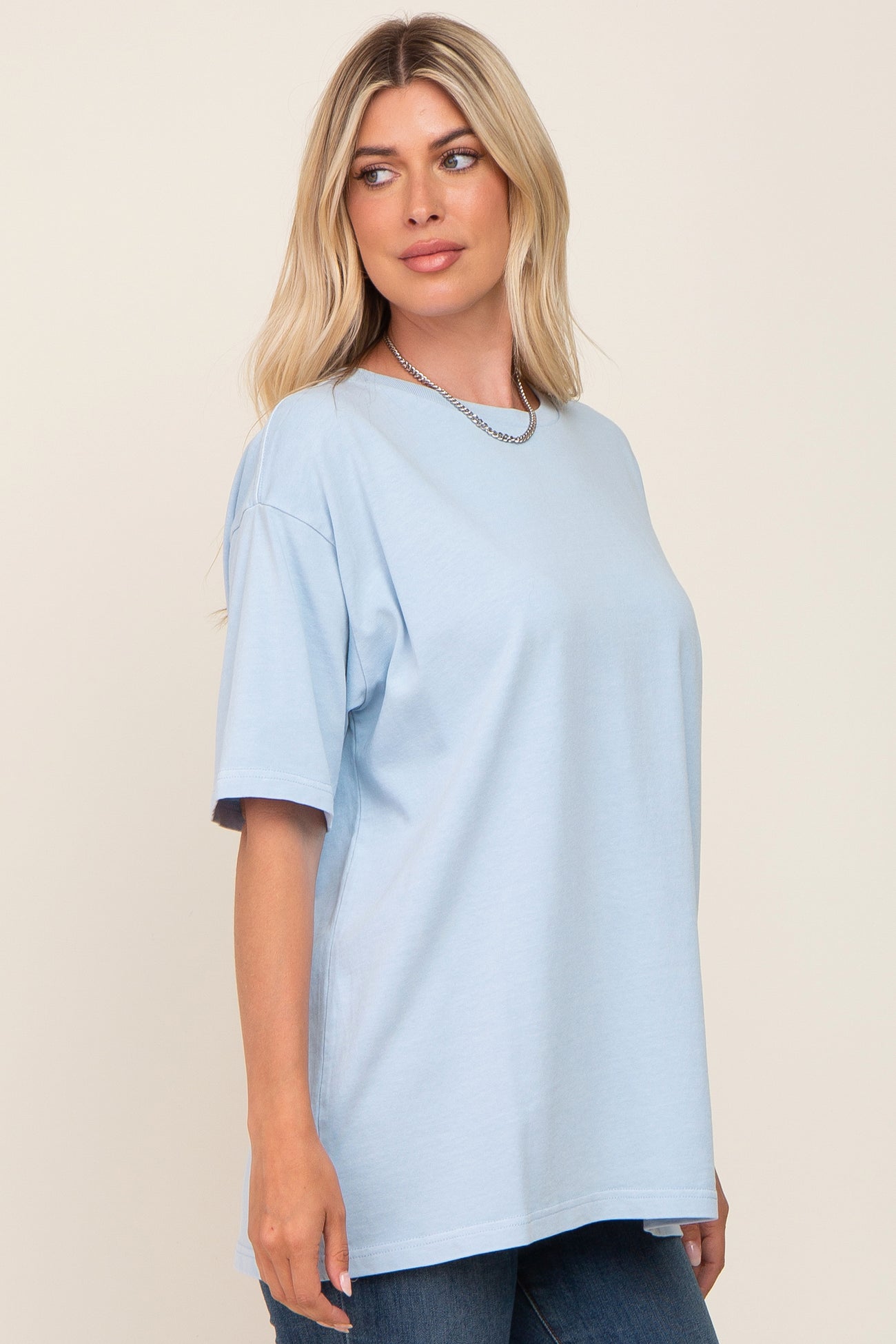 woman wearing light blue oversized t-shirt and silver chain necklace against a neutral background