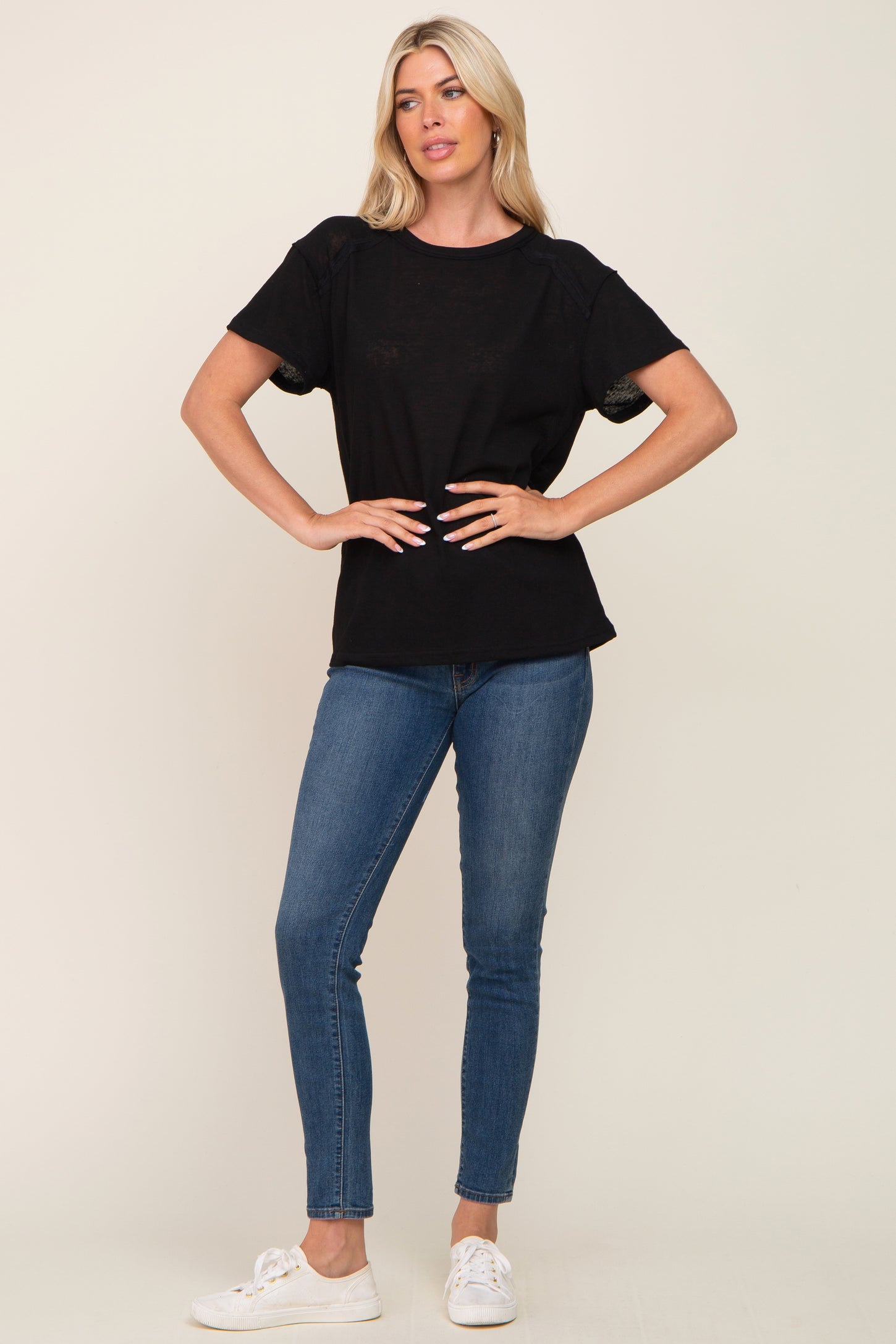 woman wearing a black short sleeve top with lace detailing, paired with blue skinny jeans and white sneakers