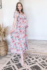 pregnant woman in floral maternity maxi dress and white strappy sandals standing in a bright room