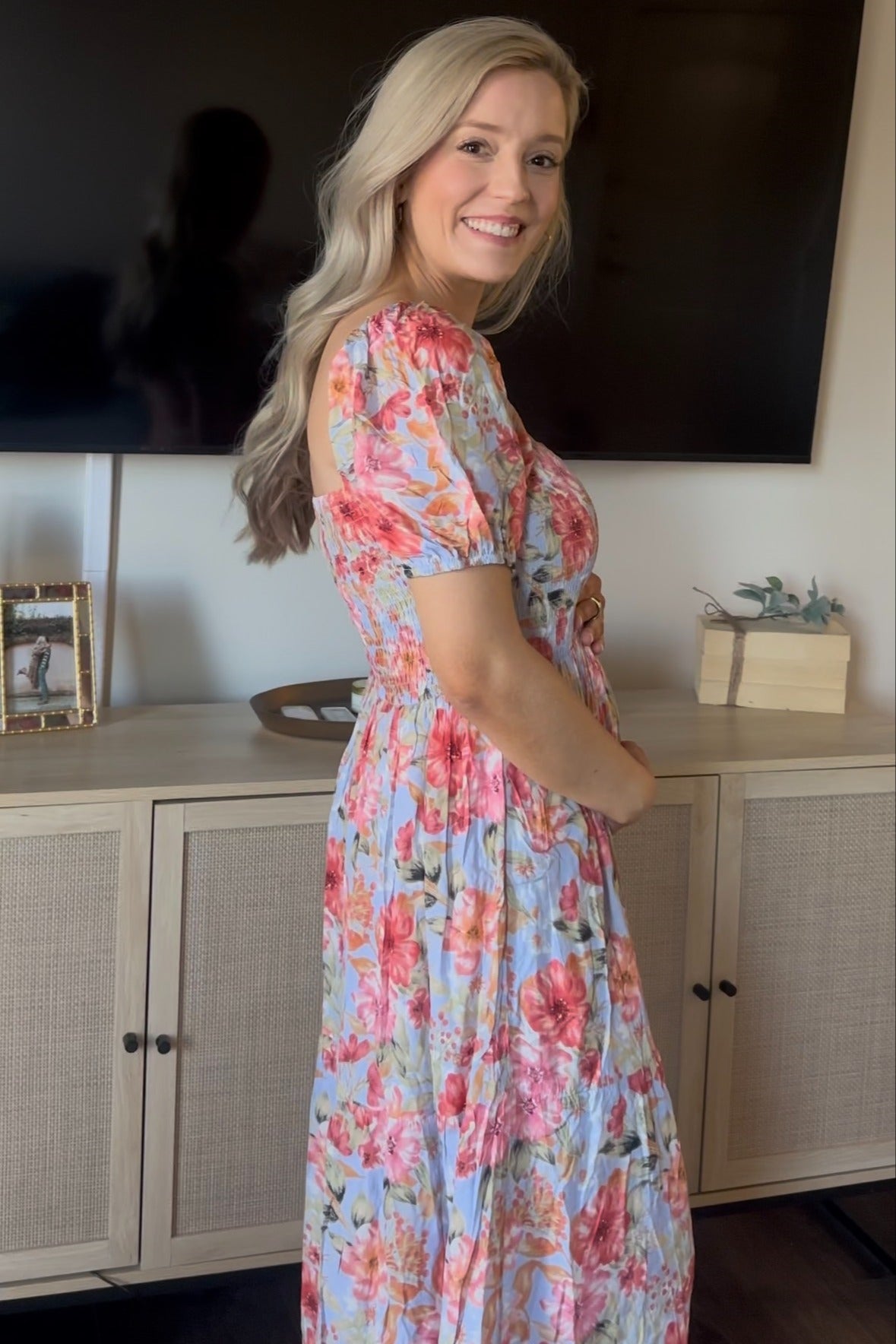 woman wearing a floral maternity maxi dress in light blue with short puff sleeves and a fitted waist, showing her baby bump