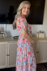 woman wearing a floral maternity maxi dress in light blue with short puff sleeves and a fitted waist, showing her baby bump