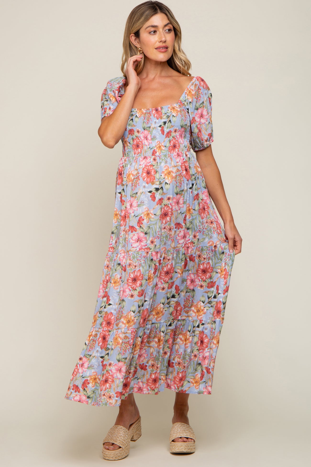 Woman wearing a light blue floral smocked maternity maxi dress with puff sleeves and woven platform sandals