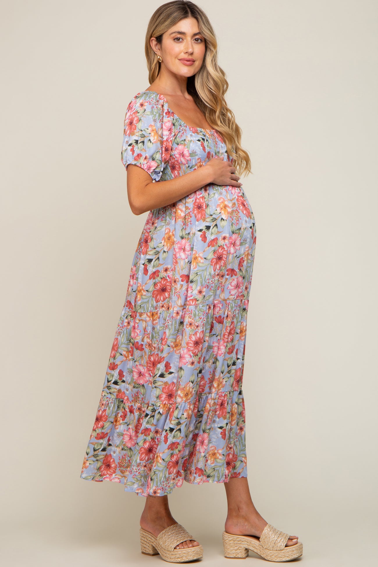 woman wearing a floral print maternity dress with puff sleeves and a tiered skirt, holding her baby bump