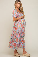 woman wearing a floral print maternity dress with puff sleeves and a tiered skirt, holding her baby bump