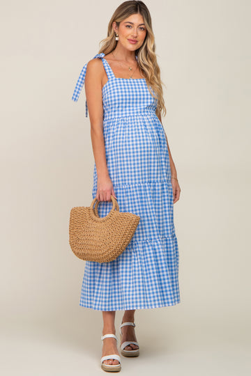 woman wearing a blue and white gingham maternity dress with a tiered design and holding a straw bag