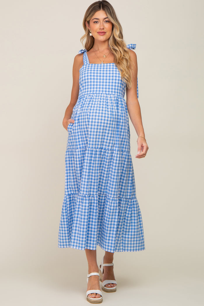 woman wearing a blue and white gingham maternity dress with tie straps and a tiered skirt, showing her baby bump