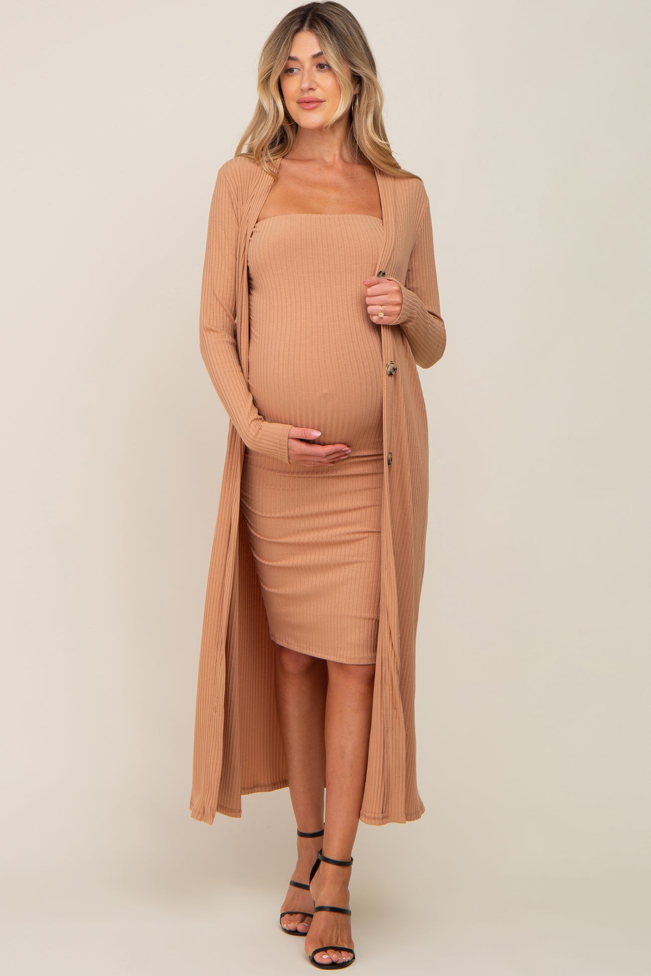 woman wearing a beige ribbed maternity dress with a matching long cardigan, holding her baby bump