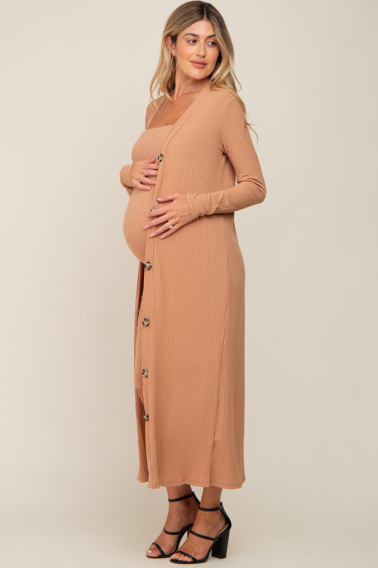 woman wearing a tan ribbed maternity dress with buttons and holding her baby bump
