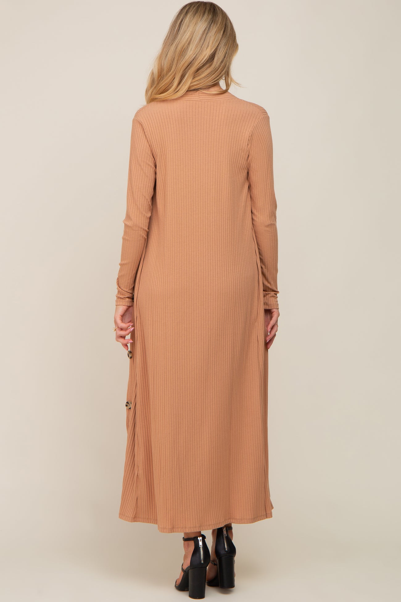 Back view of a woman wearing a long camel ribbed knit cardigan with side buttons and black heels