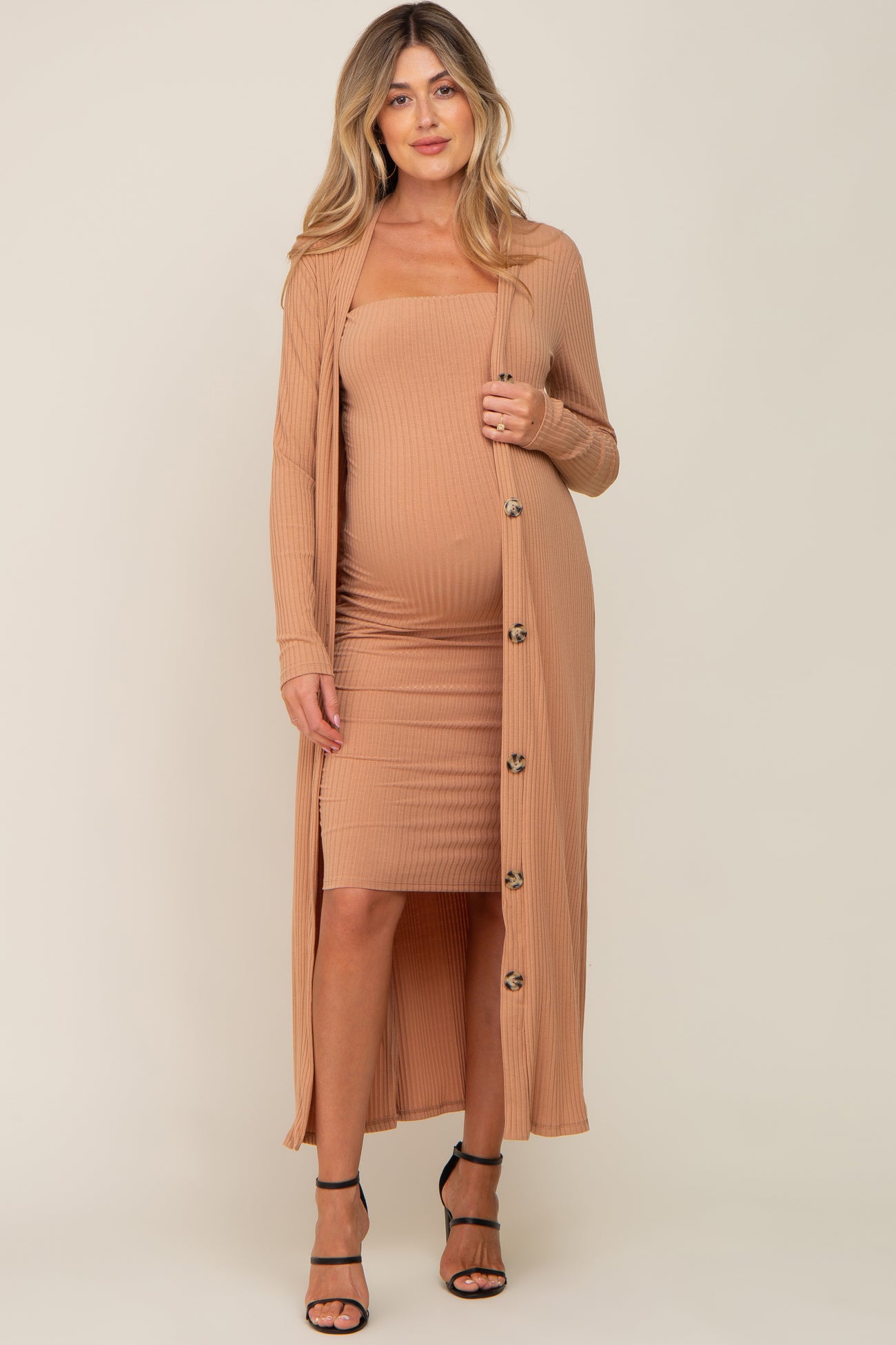 woman wearing a camel ribbed maternity dress with a matching long cardigan and showing her pregnant baby bump