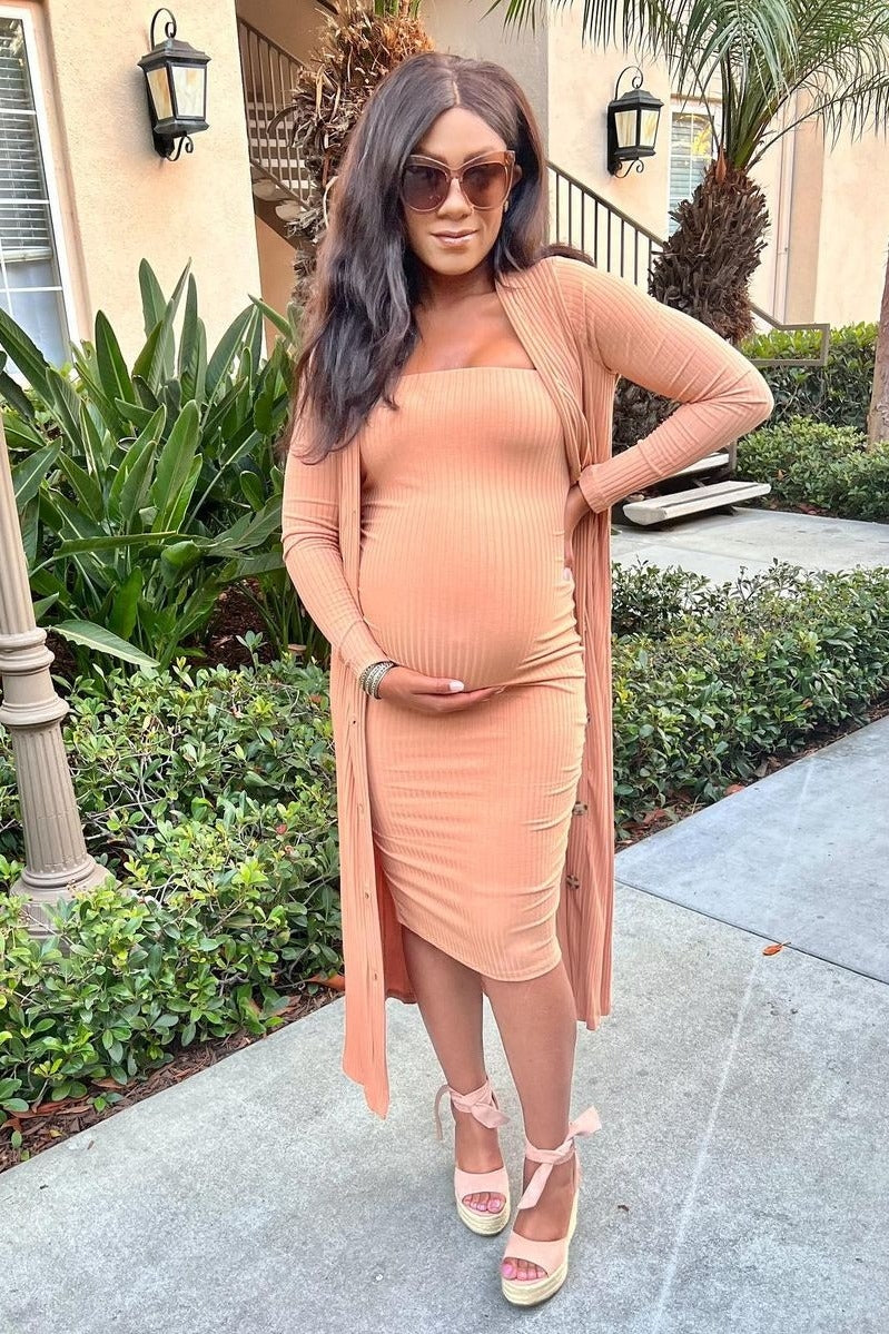 woman wearing a peach ribbed maternity dress with a matching long cardigan and holding her baby bump