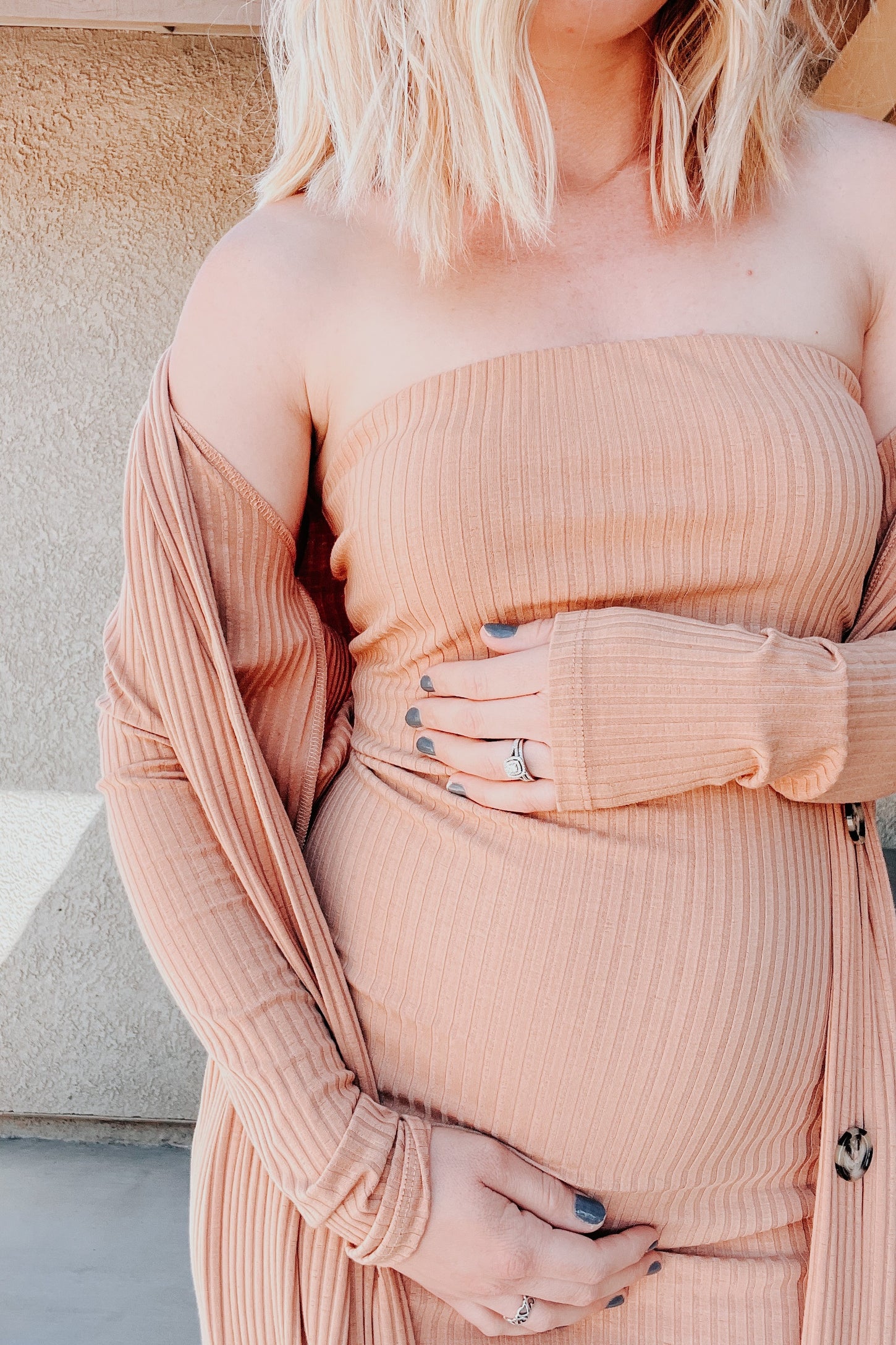 woman wearing a peach ribbed off-the-shoulder maternity dress with a long matching cardigan and holding her baby bump
