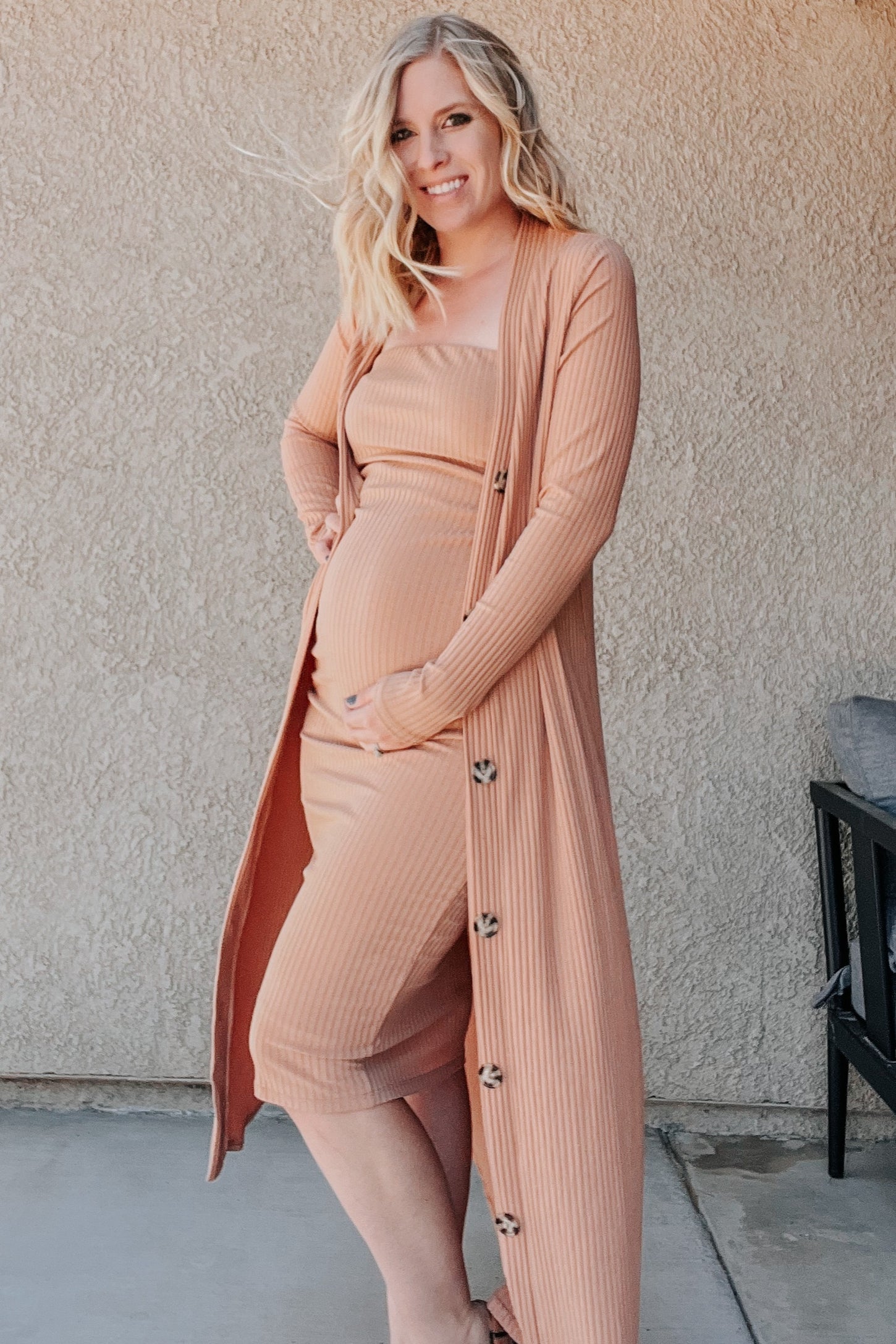 woman wearing a blush pink maternity dress with a matching long cardigan and visible baby bump
