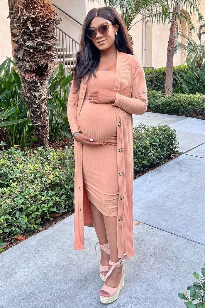 woman wearing a light pink maternity dress with a matching long cardigan, highlighting her baby bump, standing outdoors
