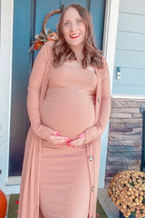 woman wearing a dusty rose ribbed maternity dress and cardigan, holding her baby bump while standing outdoors.