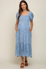 woman wearing a light blue floral maternity dress with puff sleeves and pockets, showcasing her baby bump
