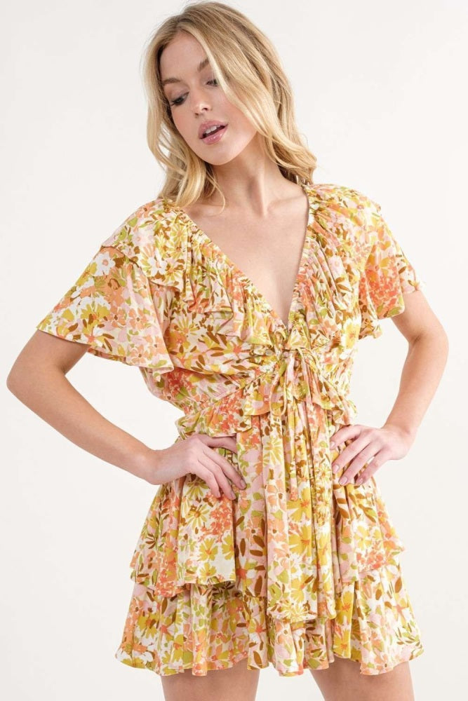 woman wearing a floral short dress with ruffled sleeves and a drawstring waist, styled with a deep v-neckline