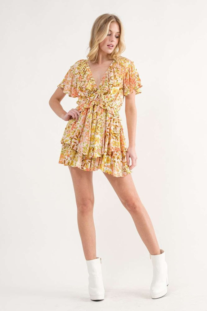 woman wearing a floral short dress with ruffled sleeves and a plunging neckline, paired with white ankle boots