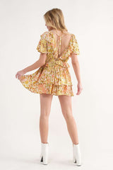 woman wearing a floral print short dress with a v-back and ruffled hem, styled with white ankle boots