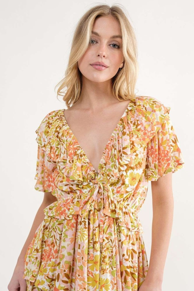 woman wearing a floral short sleeve dress with a tie front and ruffled neckline in shades of pink and orange