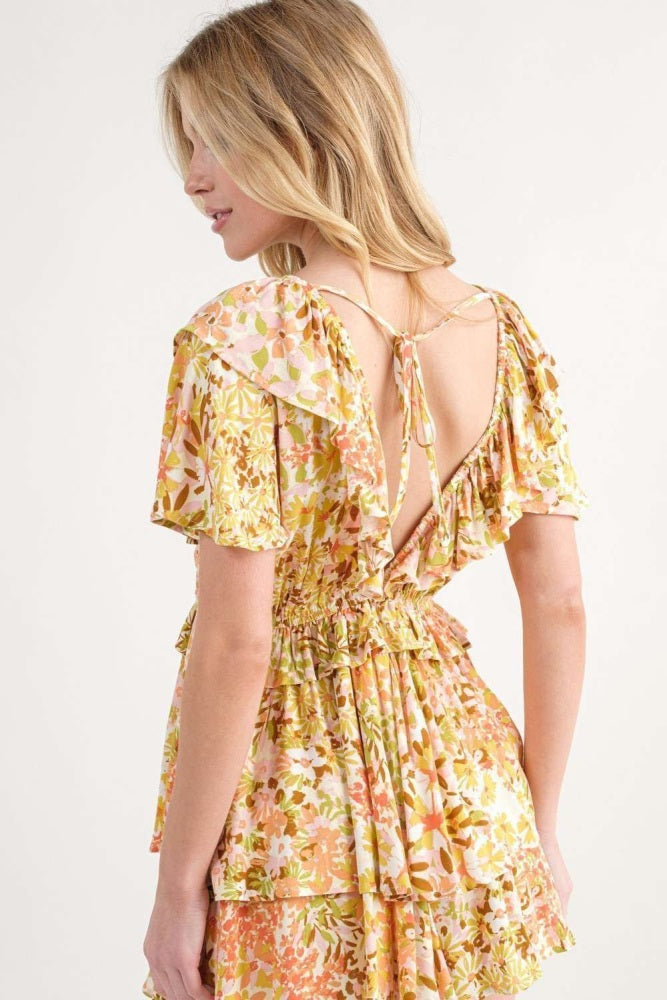 woman wearing a floral print backless dress with ruffled sleeves and a cinched waist in shades of yellow and pink