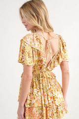 woman wearing a floral print backless dress with ruffled sleeves and a cinched waist in shades of yellow and pink