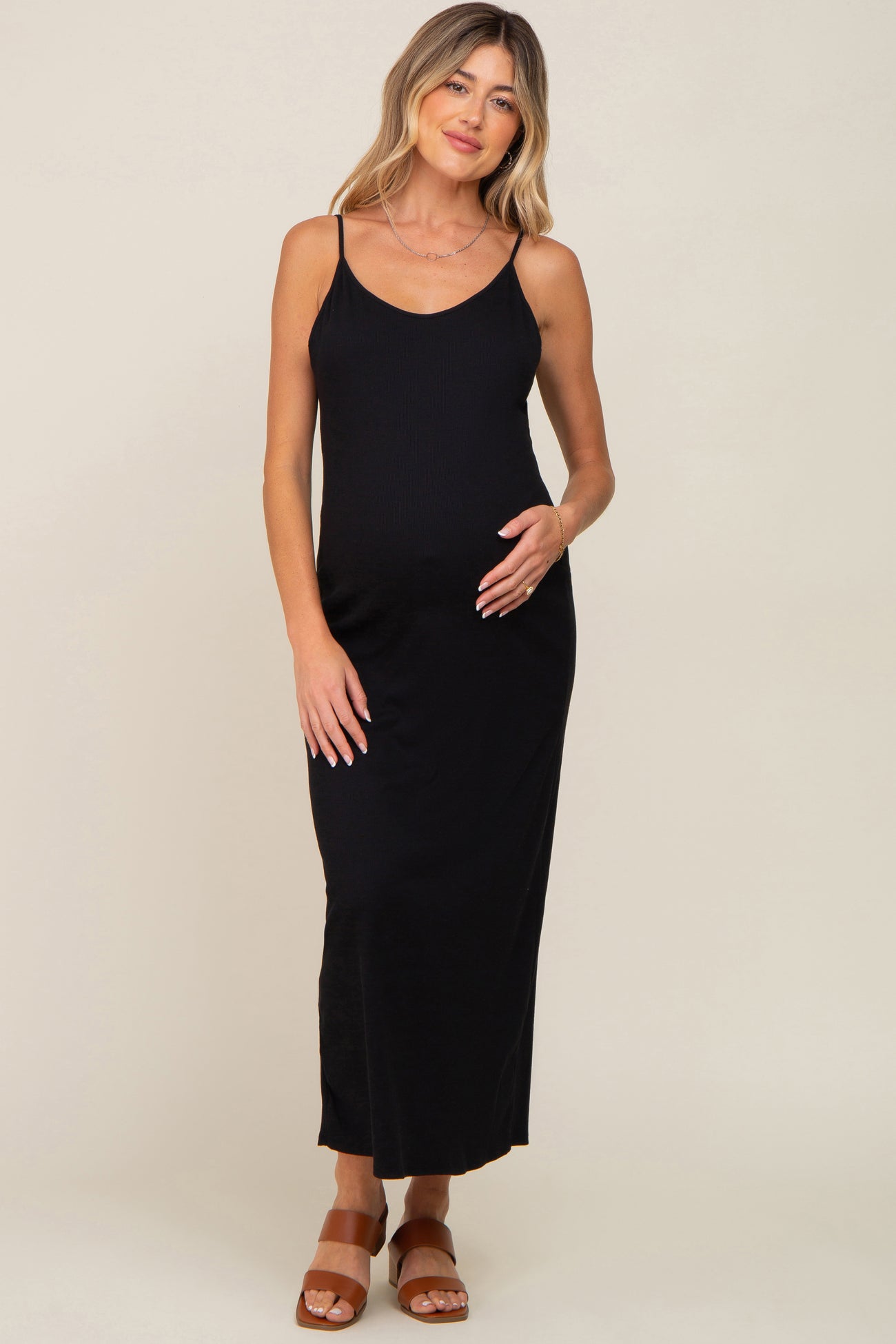woman wearing a black maternity maxi dress with adjustable straps and a visible baby bump, standing and smiling