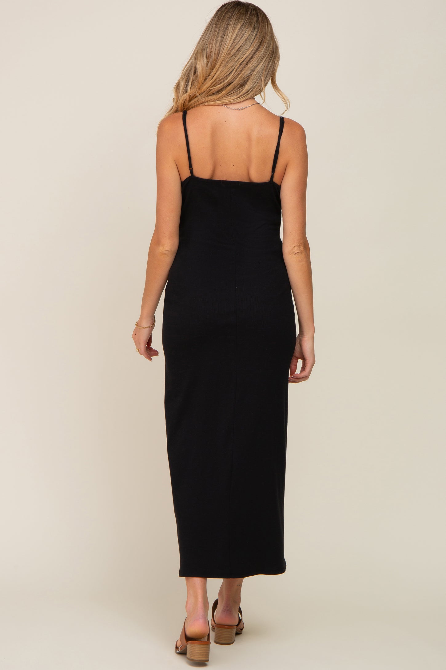 woman wearing a black maternity maxi dress with spaghetti straps, facing away, showcasing a fitted silhouette